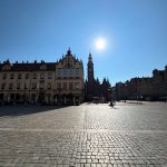 Wide angle sunny view of the historic Wrocław Market Square (Rynek) in Poland, featuring the Old Town Hall spire and colorful tenement buildings under a clear blue sky